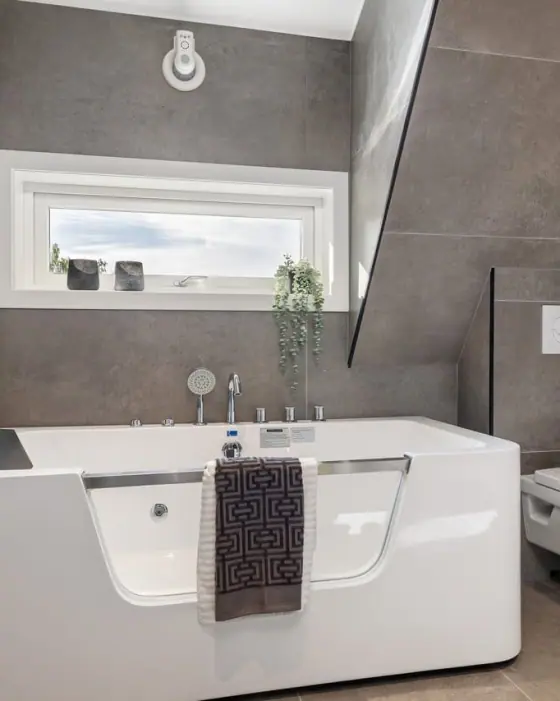 Bad under skråtak med badekar, smalt vindu og håndklestige på veggen.