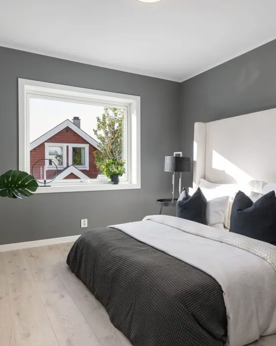 Soverom med grå vegger, dobbeltseng og vindu mot nabohuset.