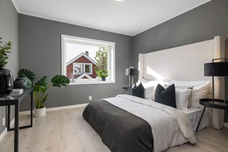 Soverom med grå vegger, dobbeltseng og vindu mot nabohuset.