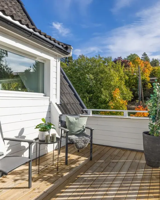 Terrasse i tre langs husveggen, med sittegruppe og hage i høstfarger.